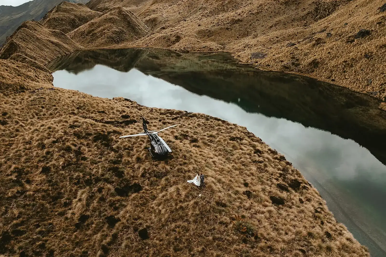 Aerial view of a helicopter landed beside an alpine tarn with the couple nearby