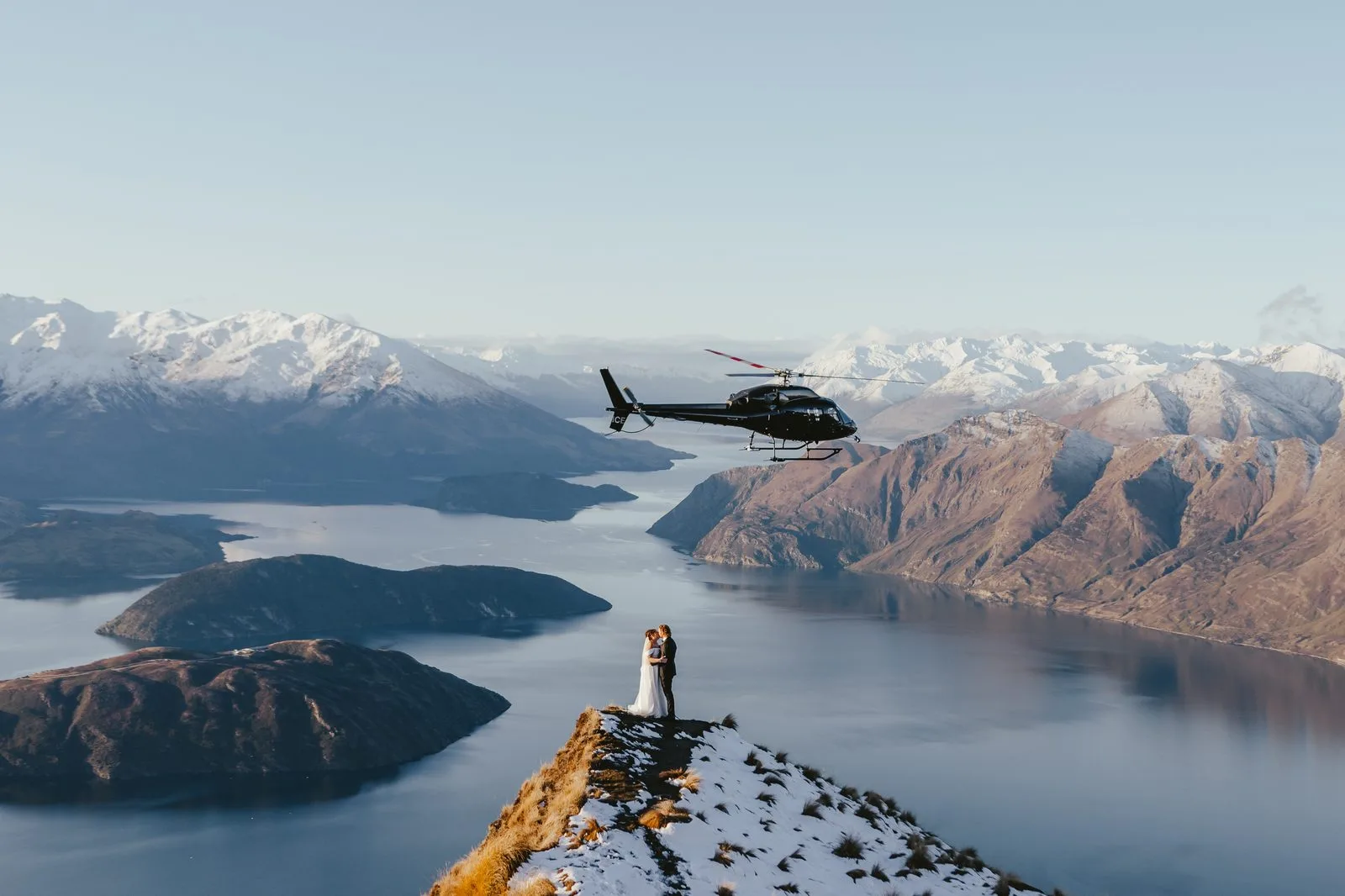 Helicopter flying past a couple standing on the Coromandel Peak ridge above Lake Wānaka
