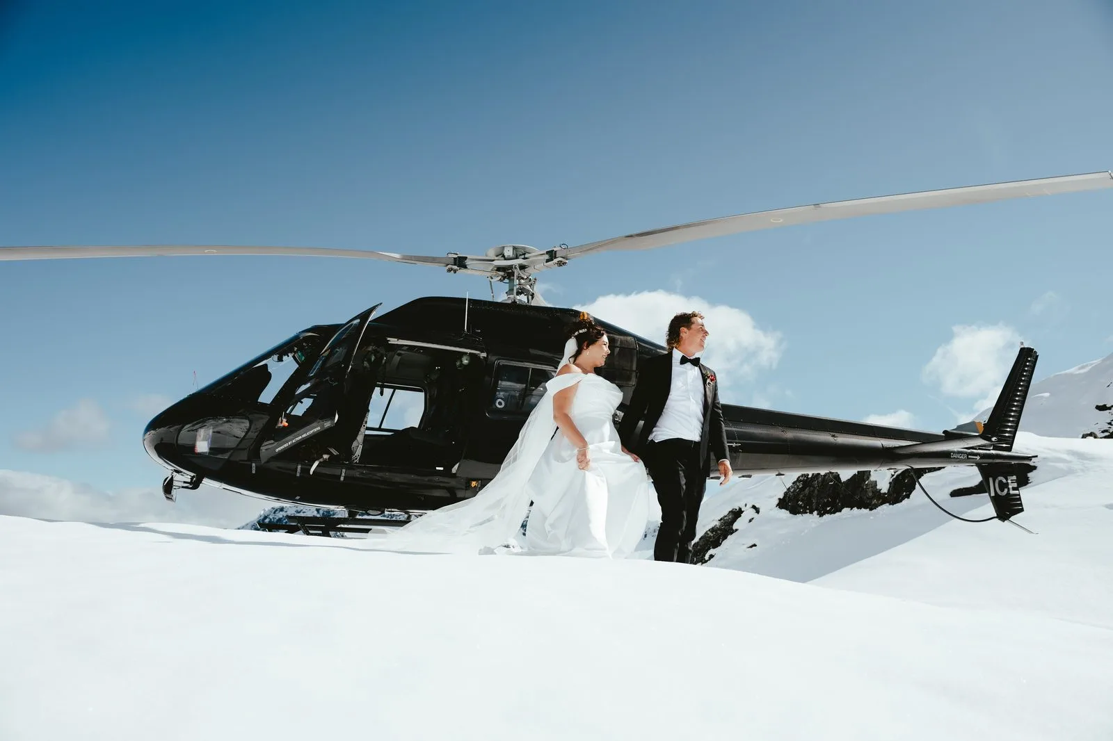 Bride and groom walking away from a parked helicopter on a snow-covered alpine landing