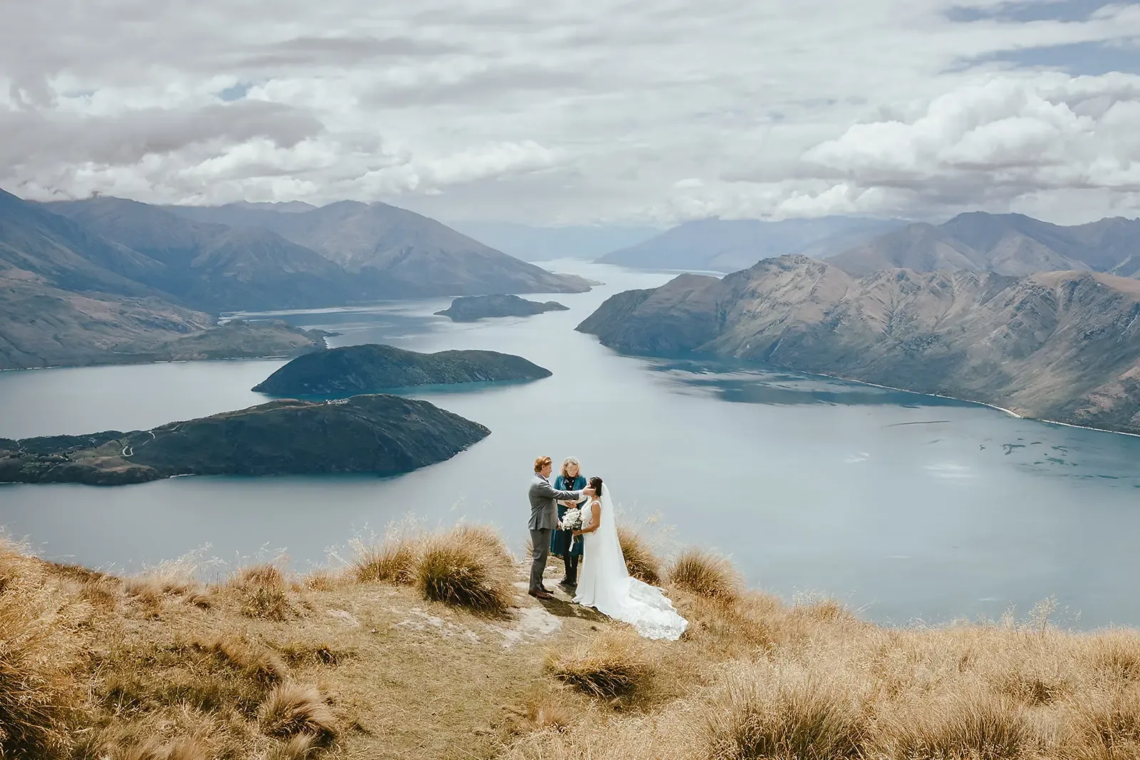 Couple exchanging vows with a celebrant, Lake Wānaka panorama behind