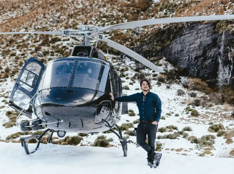 Cristian Batista beside a helicopter in snow-covered mountains