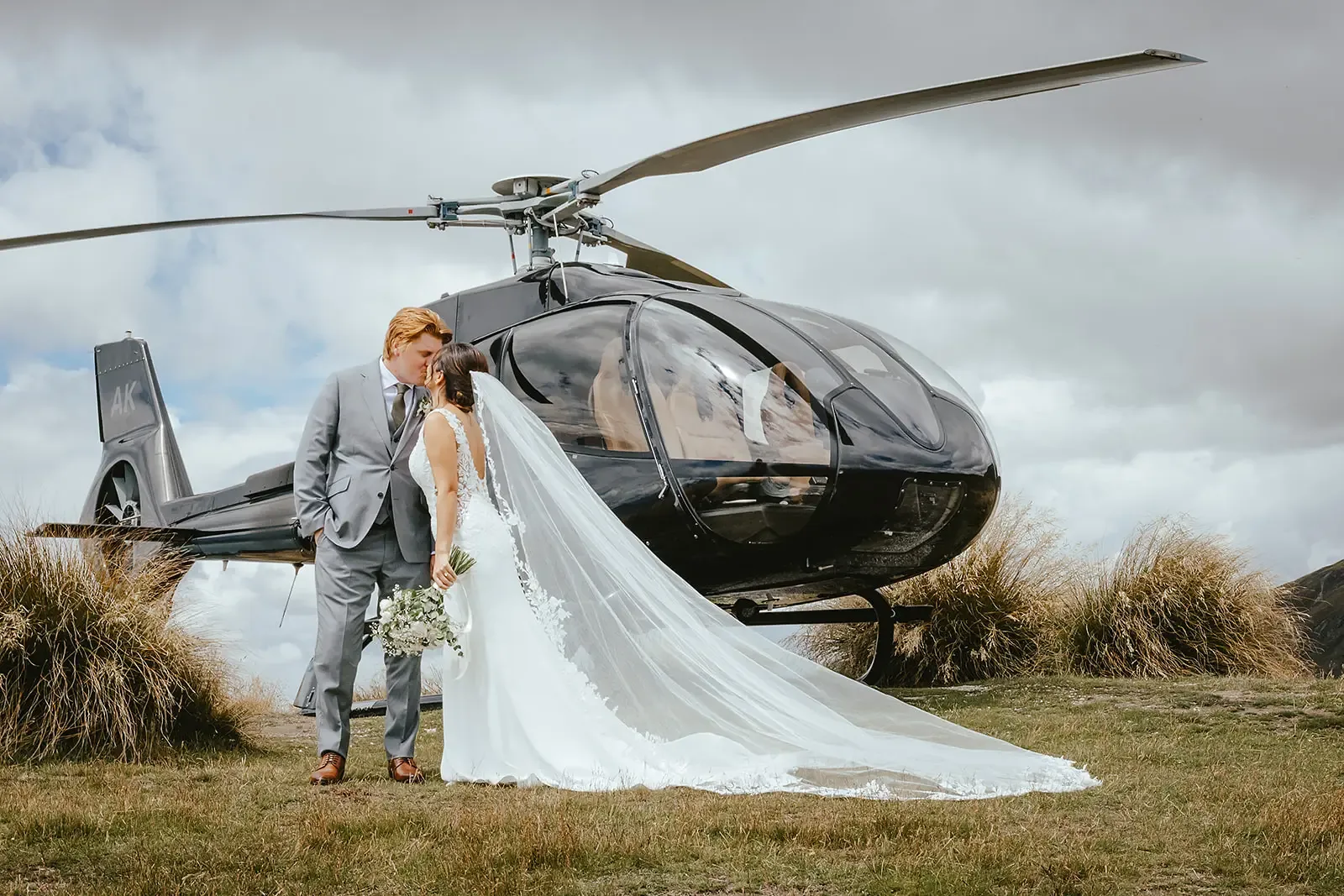 Couple kissing with the helicopter behind and the veil train extended