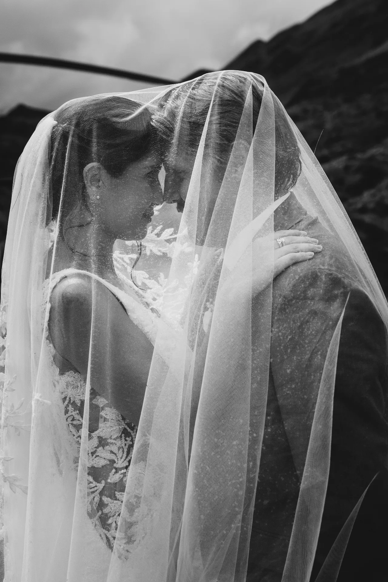 Black and white photograph of a couple kissing under the bride's veil at Alta Lakes near Wānaka