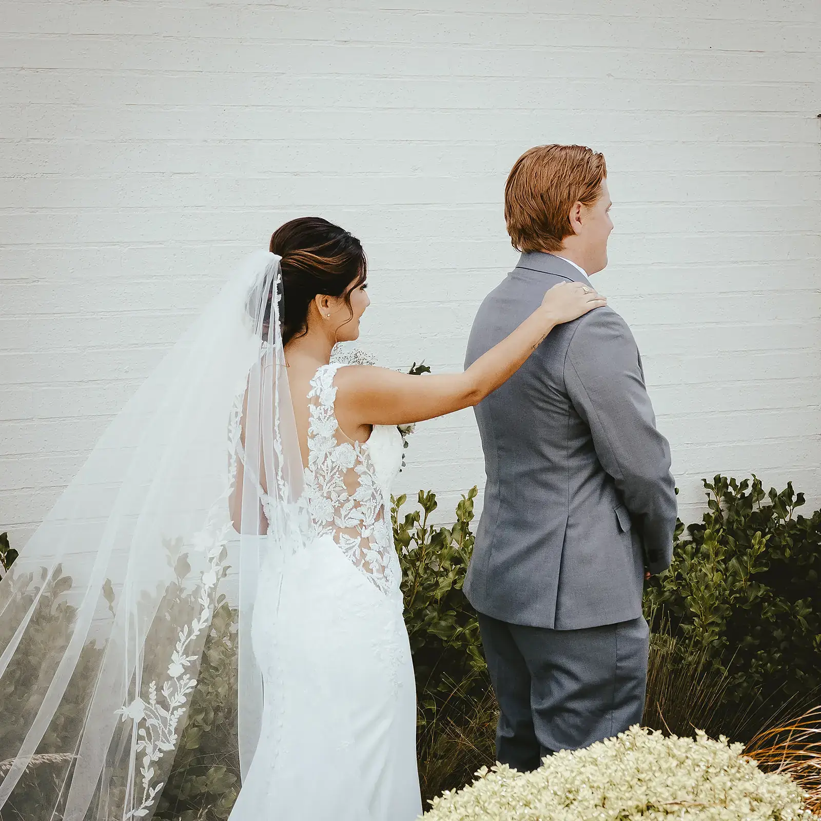 Bride in a veil resting a hand on the groom's shoulder at a garden first look