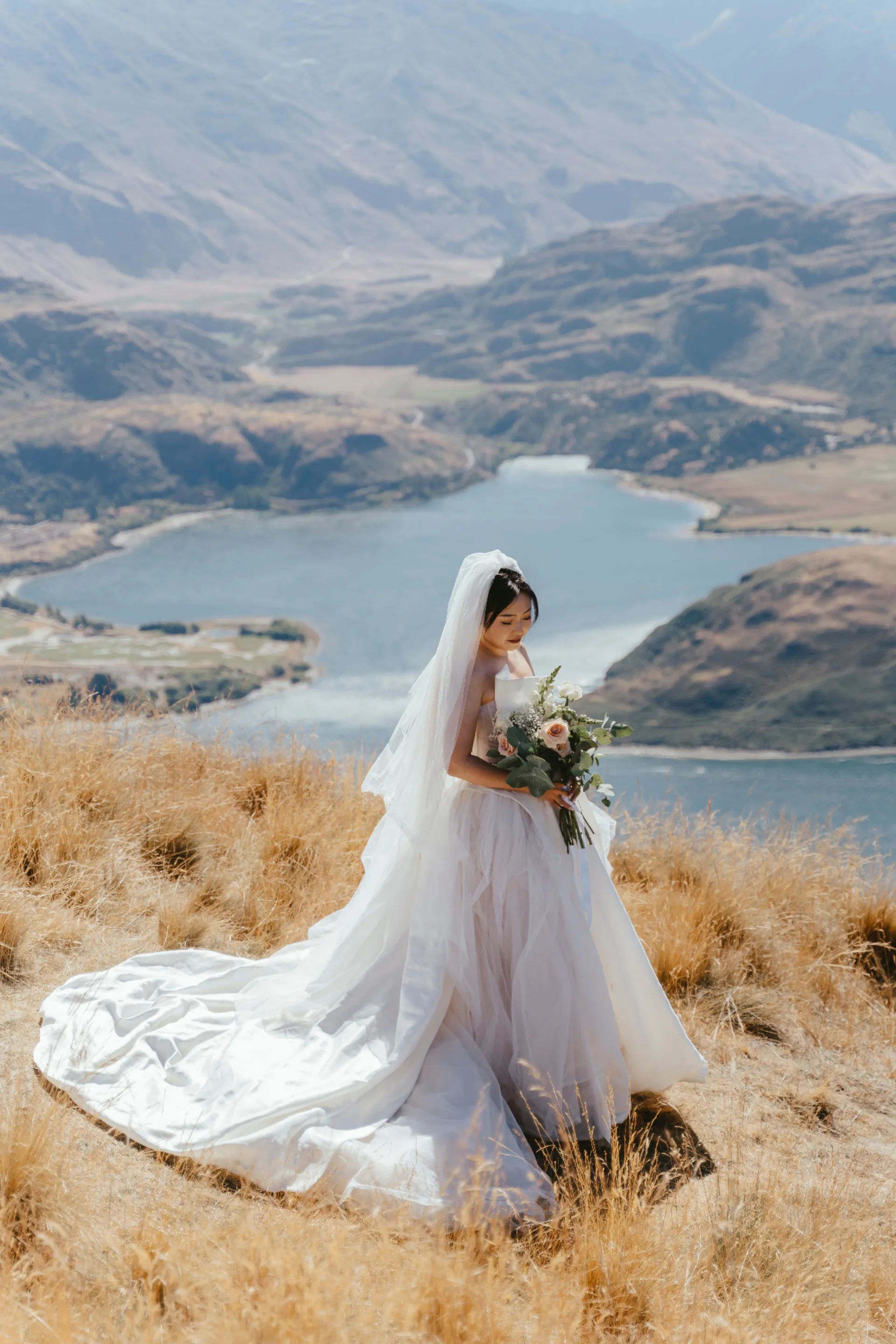 Bride holding her bouquet on a hilltop above Lake Wānaka