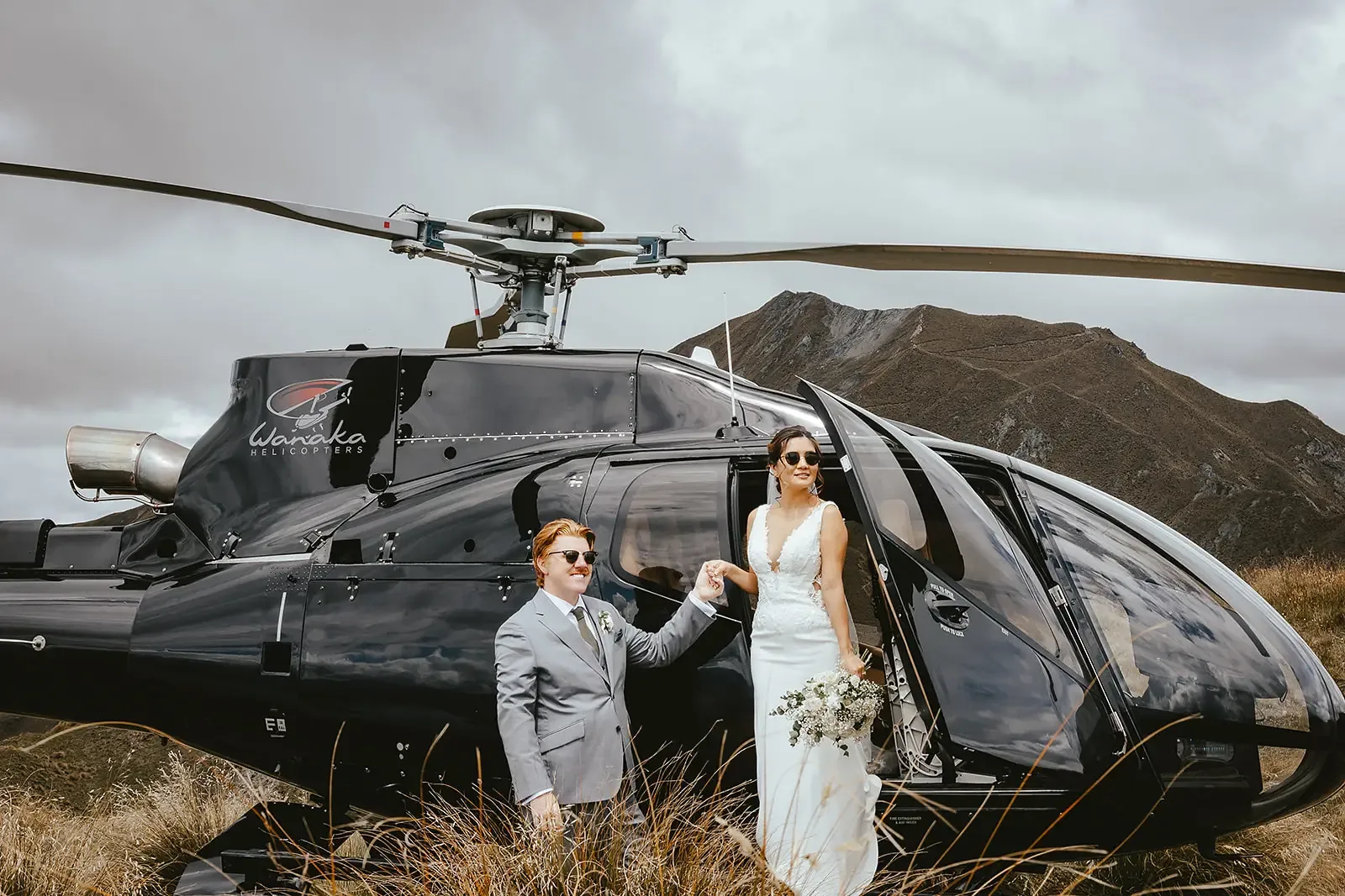 Couple in sunglasses beside a Wānaka Helicopters aircraft