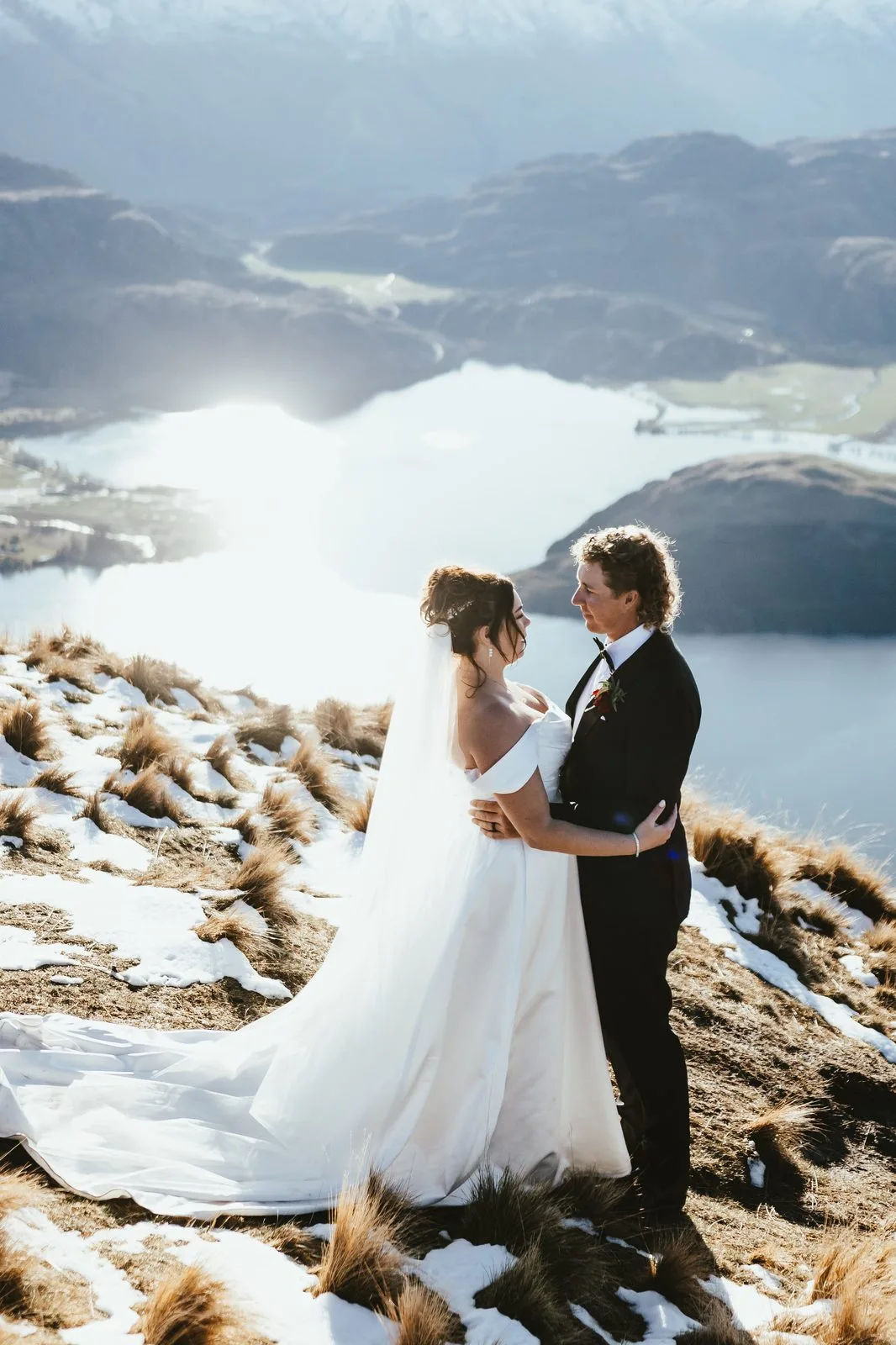Bride and groom embracing on the tussock ridge at Coromandel Peak in low golden light above Lake Wānaka