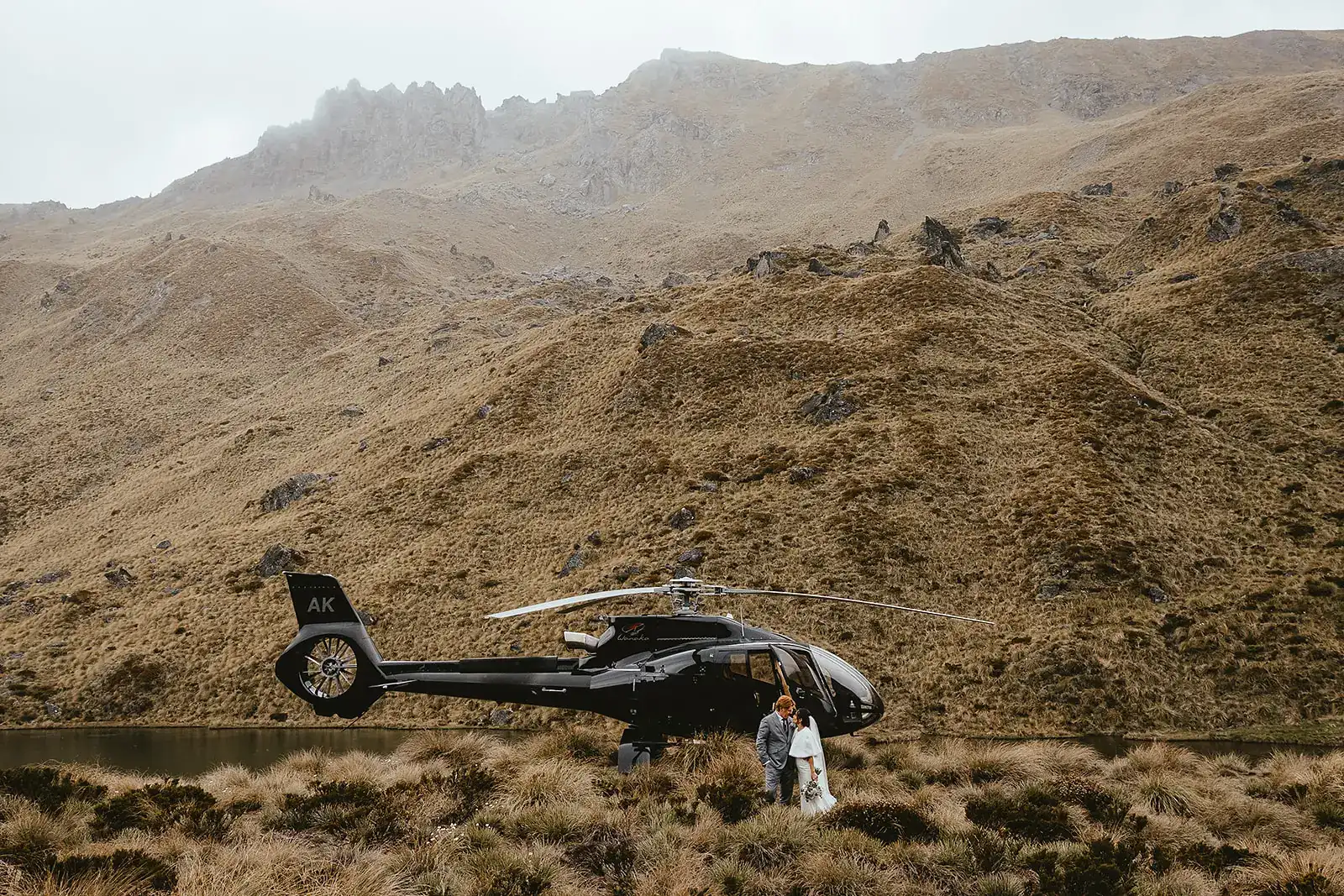 Bride and groom standing beside a helicopter in a mountain landscape