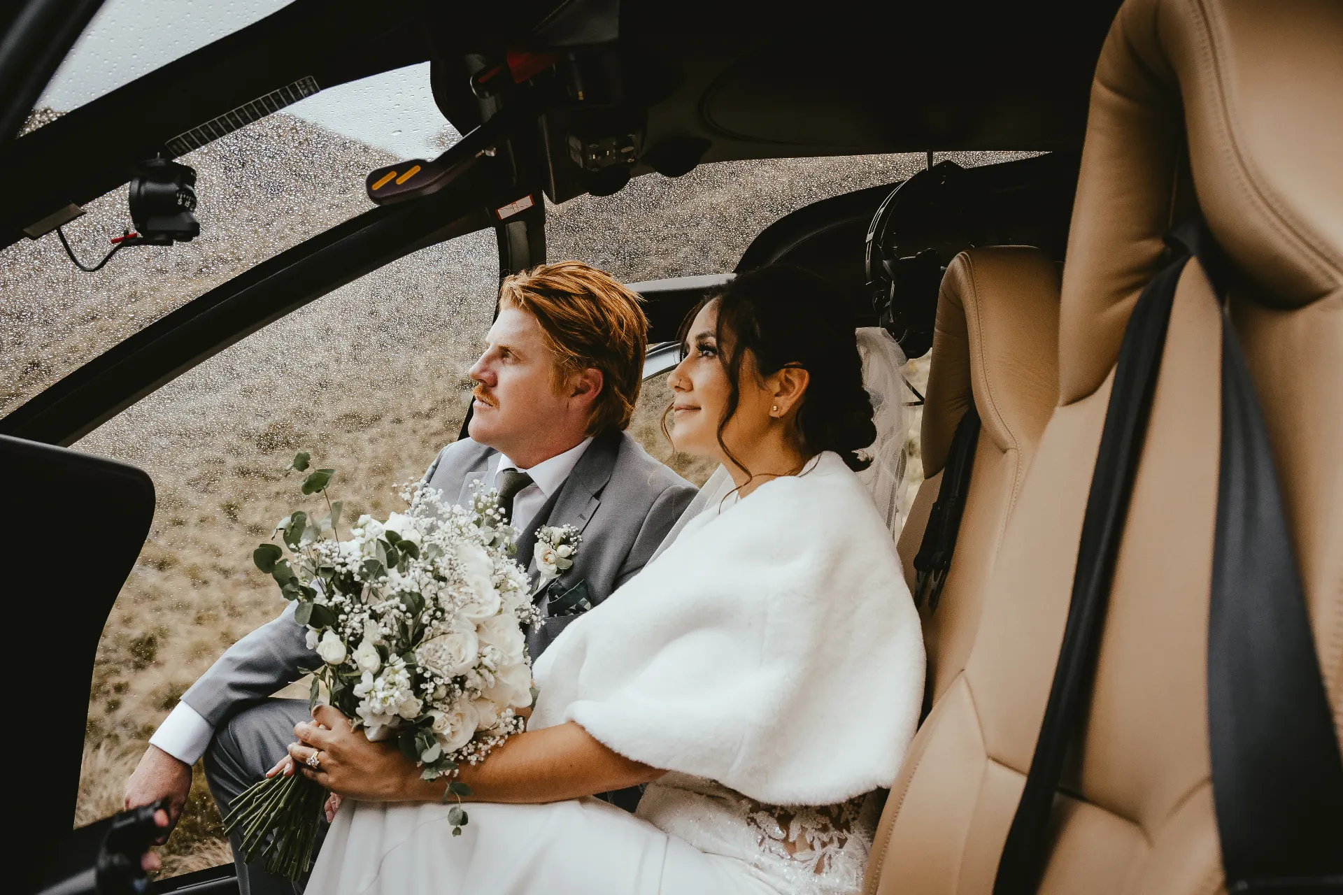 Bride and groom seated inside a helicopter cabin with her bouquet after an Alta Lakes wedding near Wānaka