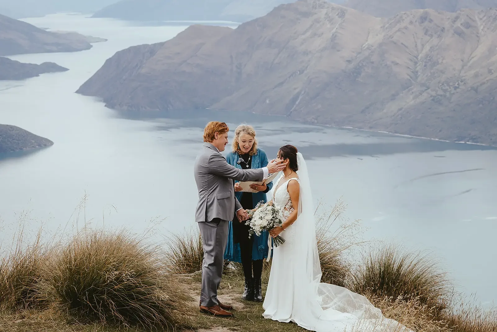 Groom touching the bride's face during the ceremony above Lake Wānaka