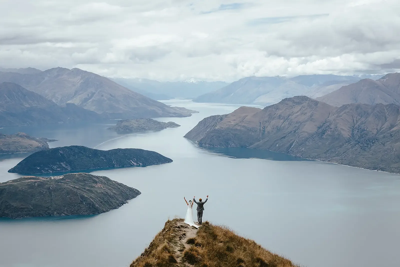 Couple with arms raised in celebration above Lake Wānaka