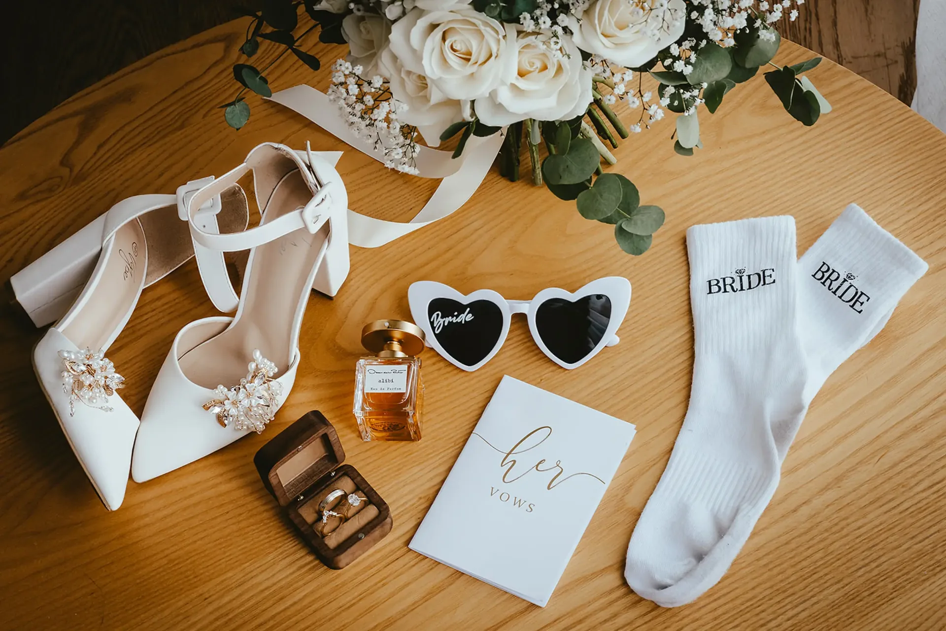 Flatlay of bridal shoes, perfume, rings and bouquet