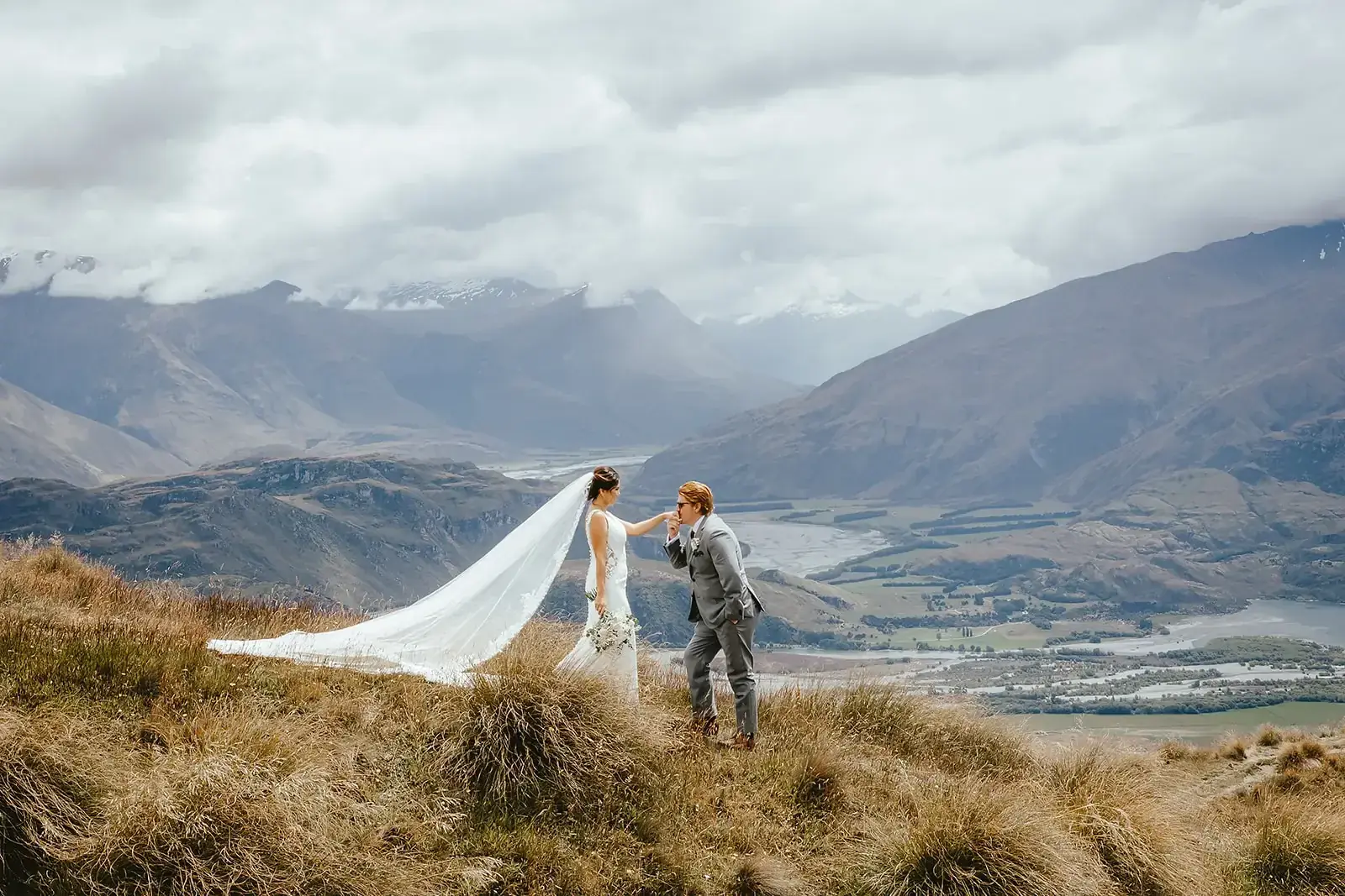 Groom kissing the bride's hand with mountain valley behind